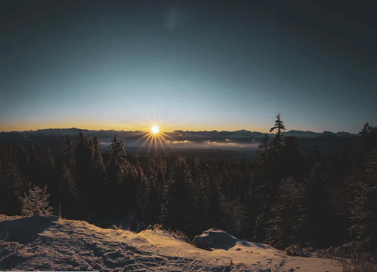 Coucher de soleil éclatant sur les forêts enneigées du Jura, invitation à l'aventure.