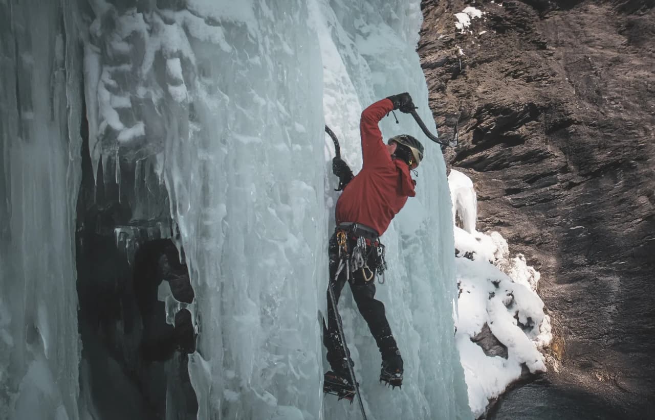 Un grimpeur s'attaque à une cascade de glace majestueuse, entouré de paysages alpins enchanteurs.