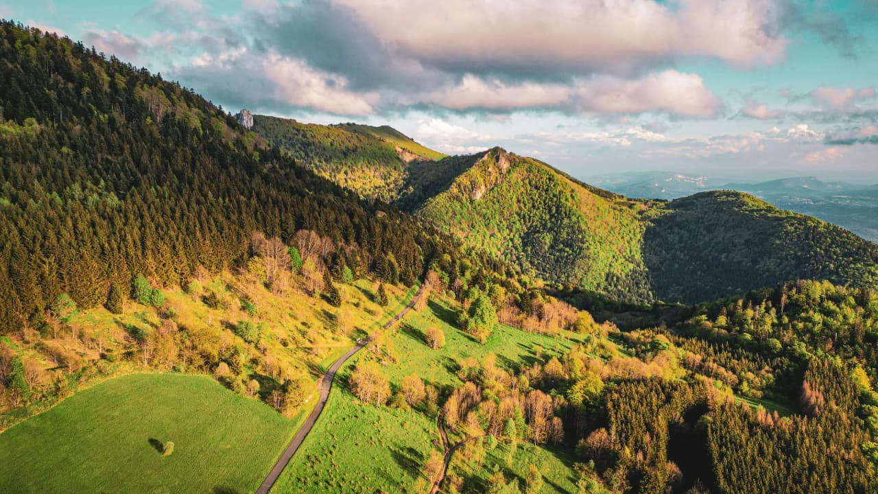 The lush green landscape of the Jura, valleys and mountains under a luminous sky, an invitation to adventure.