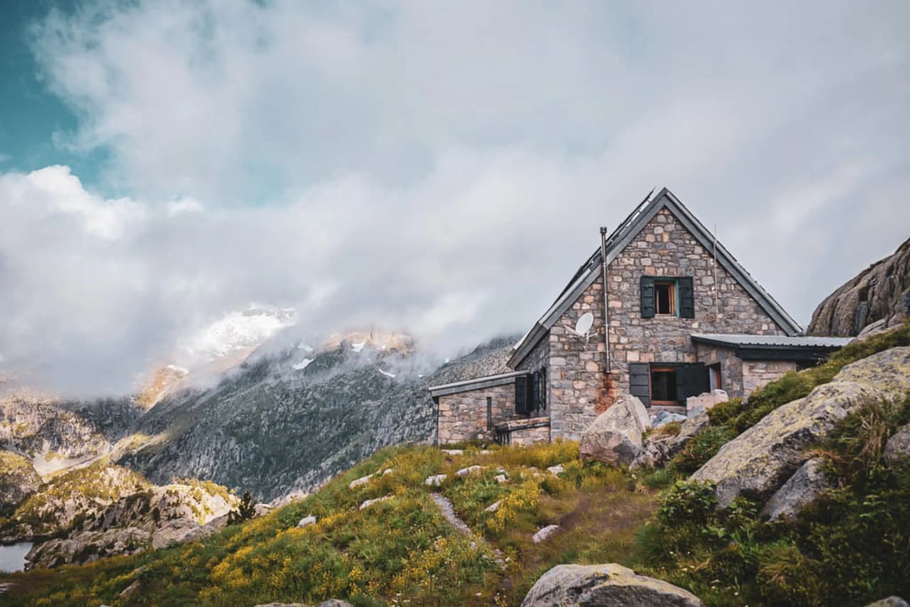A picturesque stone Mountain hut surrounded by majestic mountains and flower-filled valleys.