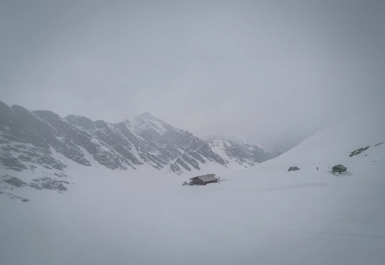 Un paysage hivernal majestueux, avec des montagnes enneigées et un refuge accueillant au milieu.