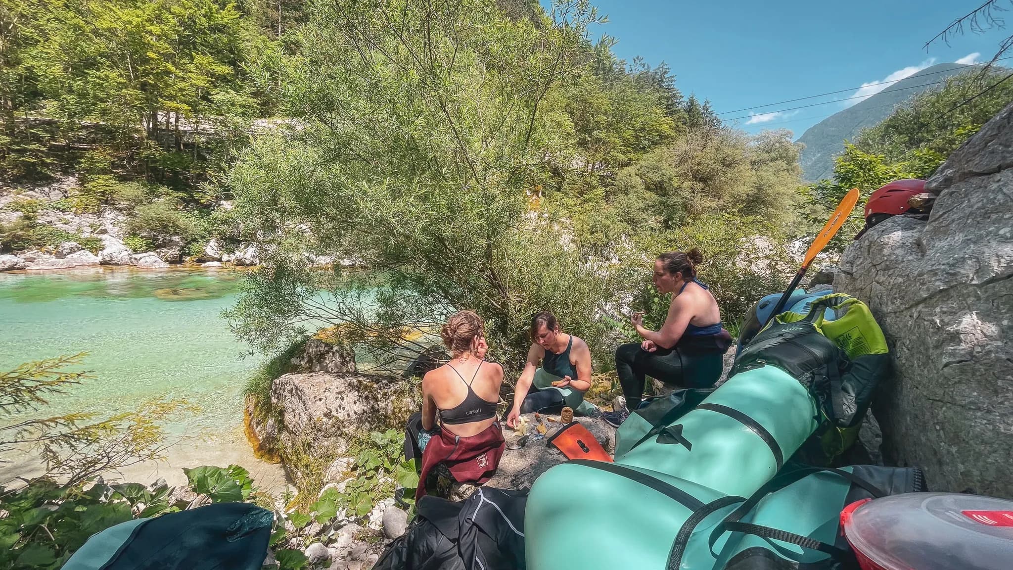 Trois personnes se reposent au bord d'une rivière turquoise, entourées de nature verdoyante.