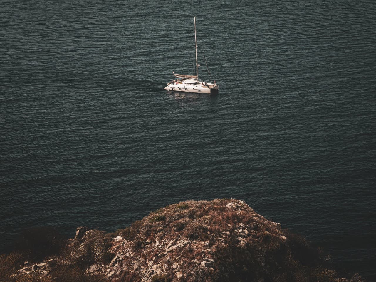 Un catamaran naviguant calmement sur les eaux turquoise près d'une côte rocheuse en Corse.