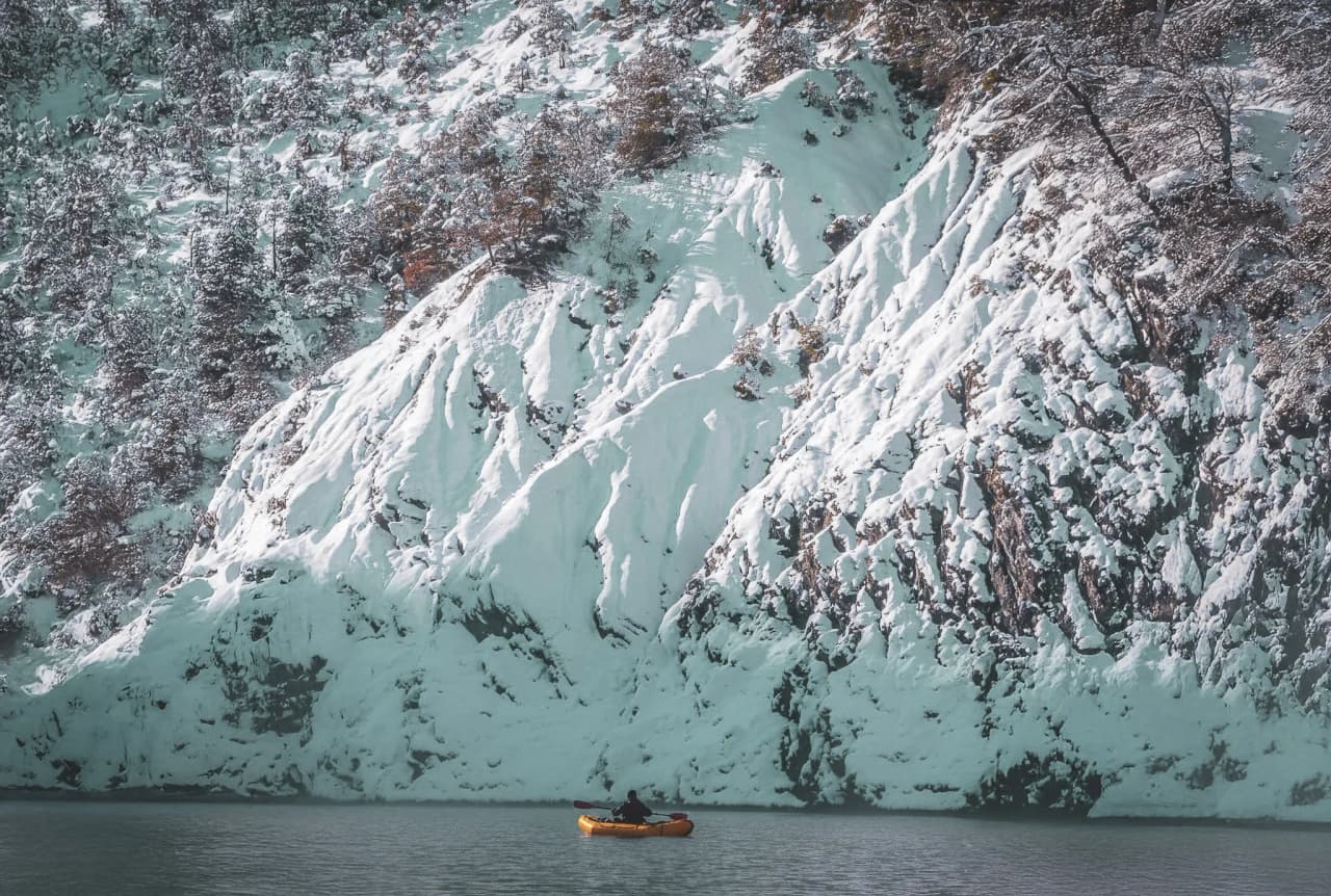 Kayak orange sur le lac gelé, bordé de falaises enneigées, paysage hivernal à couper le souffle.