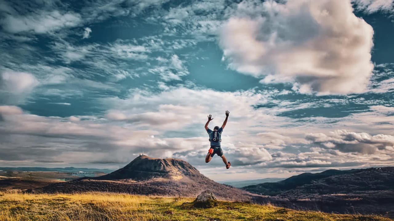 An athlete in full jump over a majestic volcanic landscape in the Auvergne, a living sky.