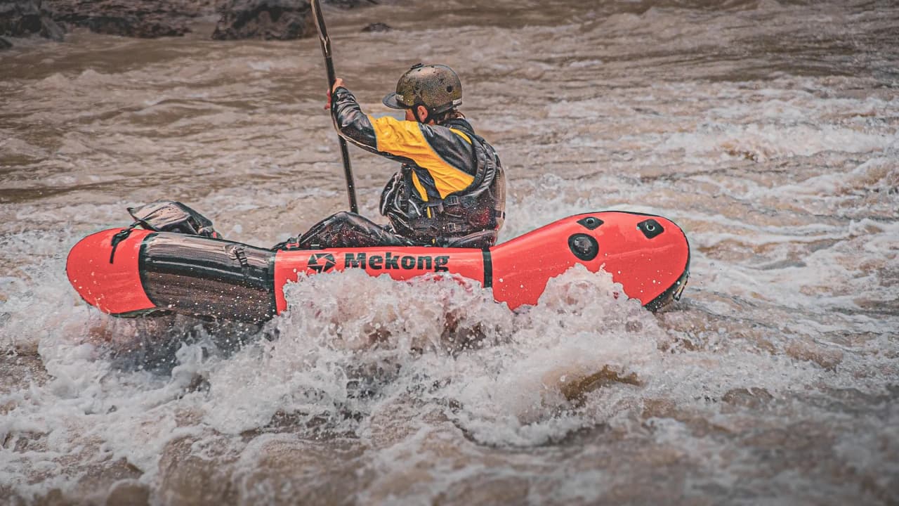 Een roeier in een rode packraft vaart door stroomversnellingen, omringd door bergen en wateravontuur.