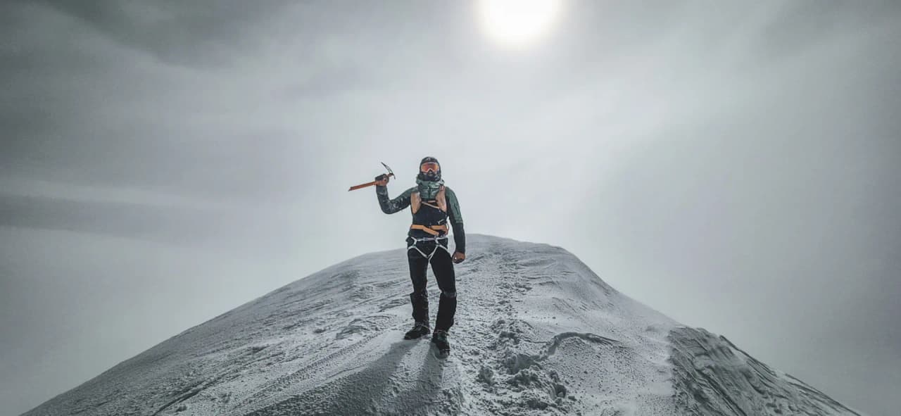 Un randonneur acclamant l'ascension au sommet enneigé du Mont Blanc, sous un ciel nuageux.