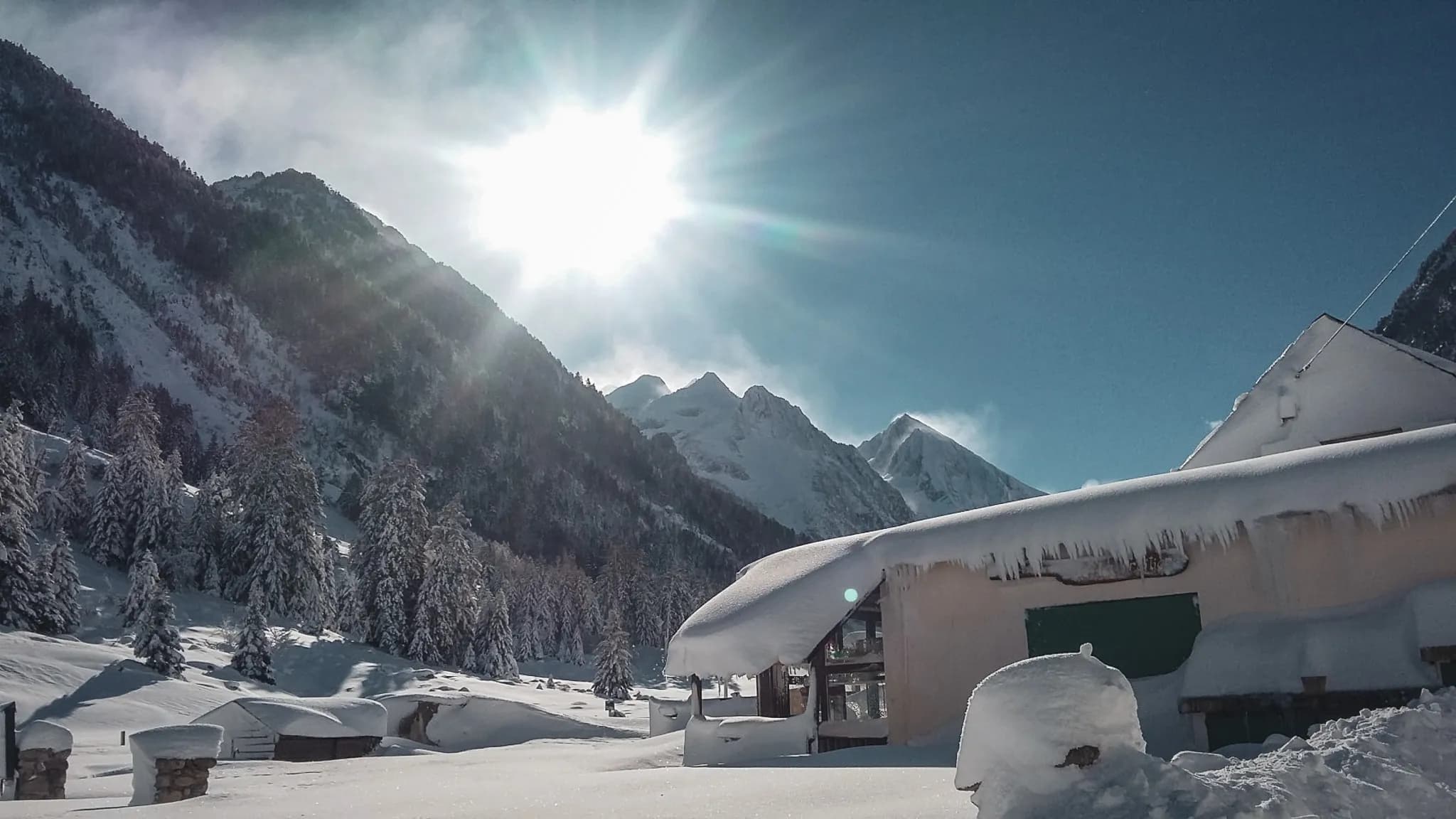 An enchanting Mountain hut under sunny skies, surrounded by majestic snow-covered landscapes.