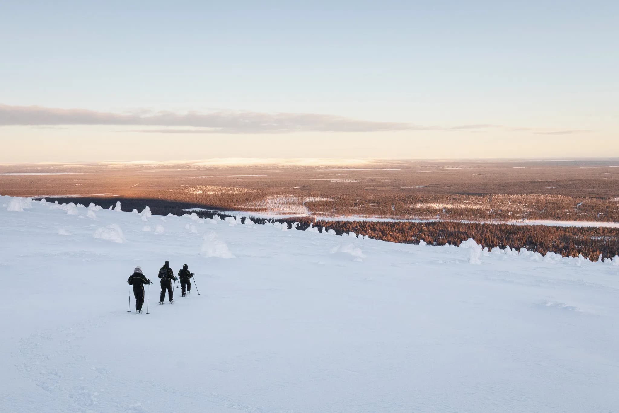 Trois randonneurs en raquettes sur un vaste paysage enneigé, face à une vallée majestueuse.