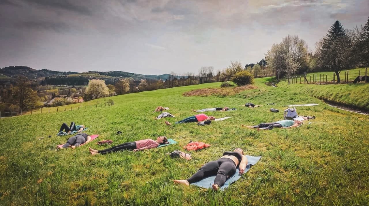 Participants relax on mattresses in a green field, under a serene sky.