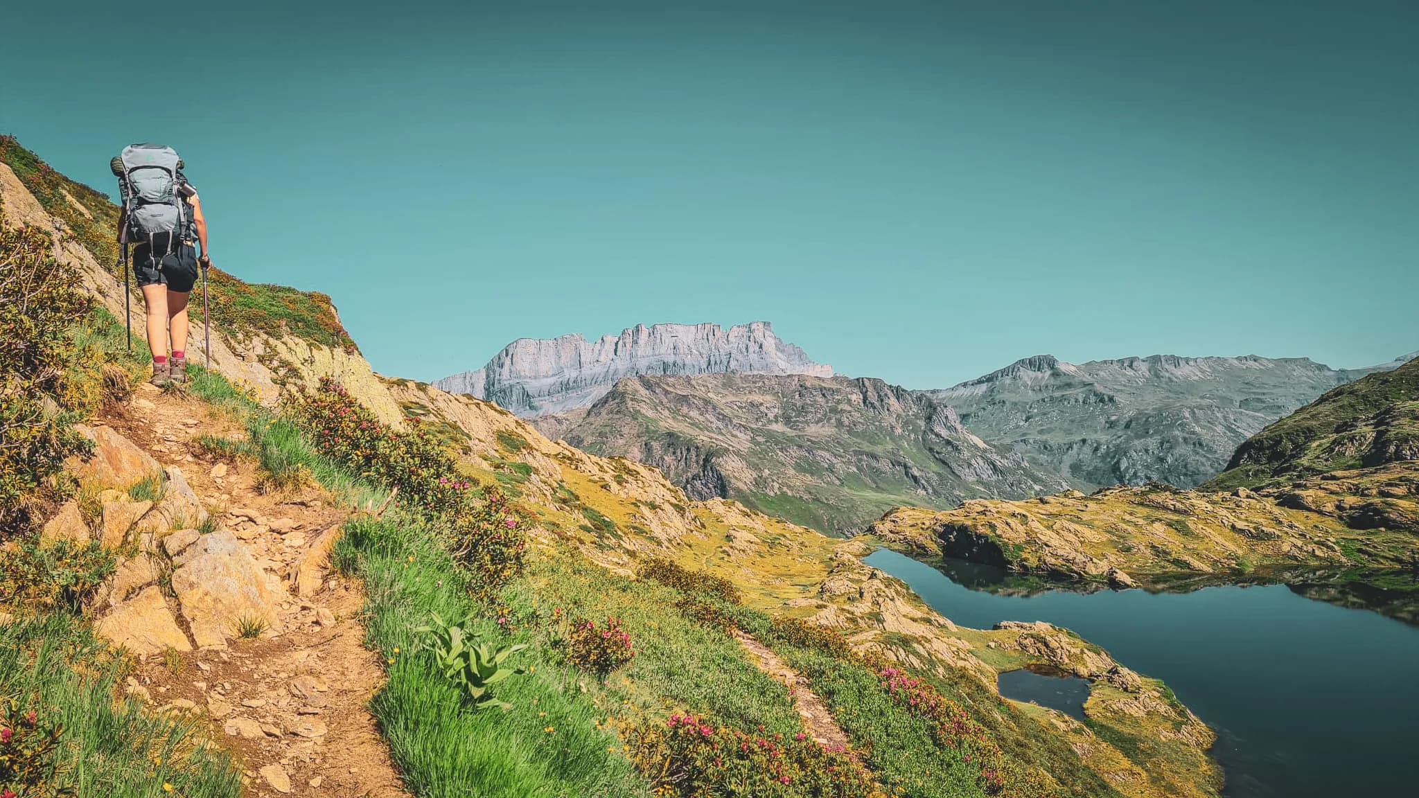 Un randonneur explore un sentier pittoresque entouré de montagnes et de lacs enchanteurs.