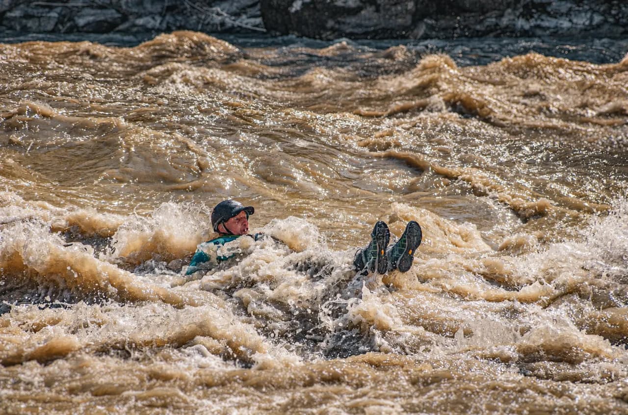 Een avonturier glijdt door de woeste stroomversnellingen van een rivier, omringd door bruisend en schuimend water.