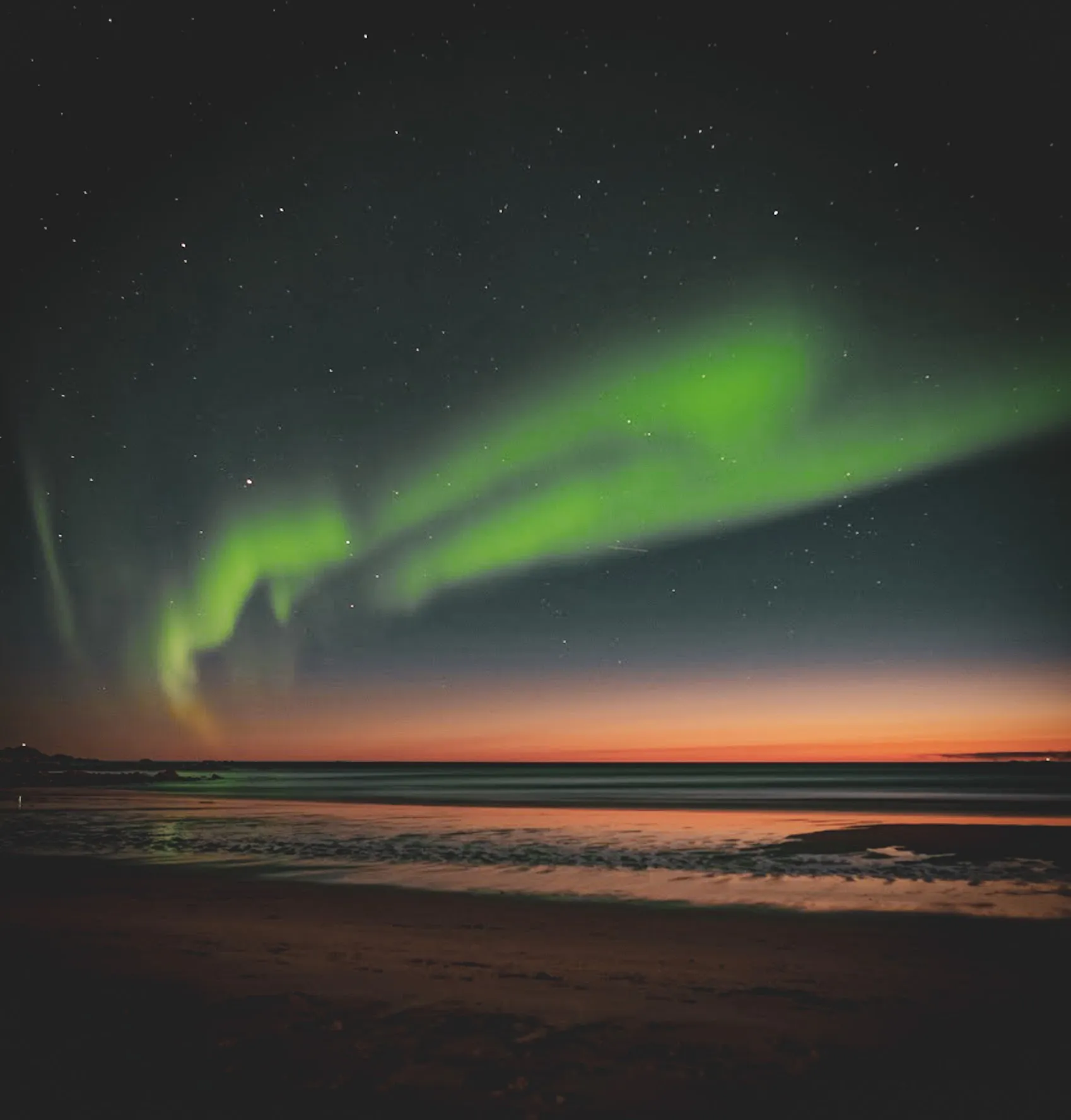 Northern lights in a starry sky on the beach, magical reflections on the waves.