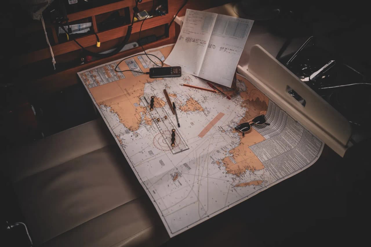 Carte nautique déployée sur un cockpit, entourée de stylos et accessoires marins, évoquant l'aventure.