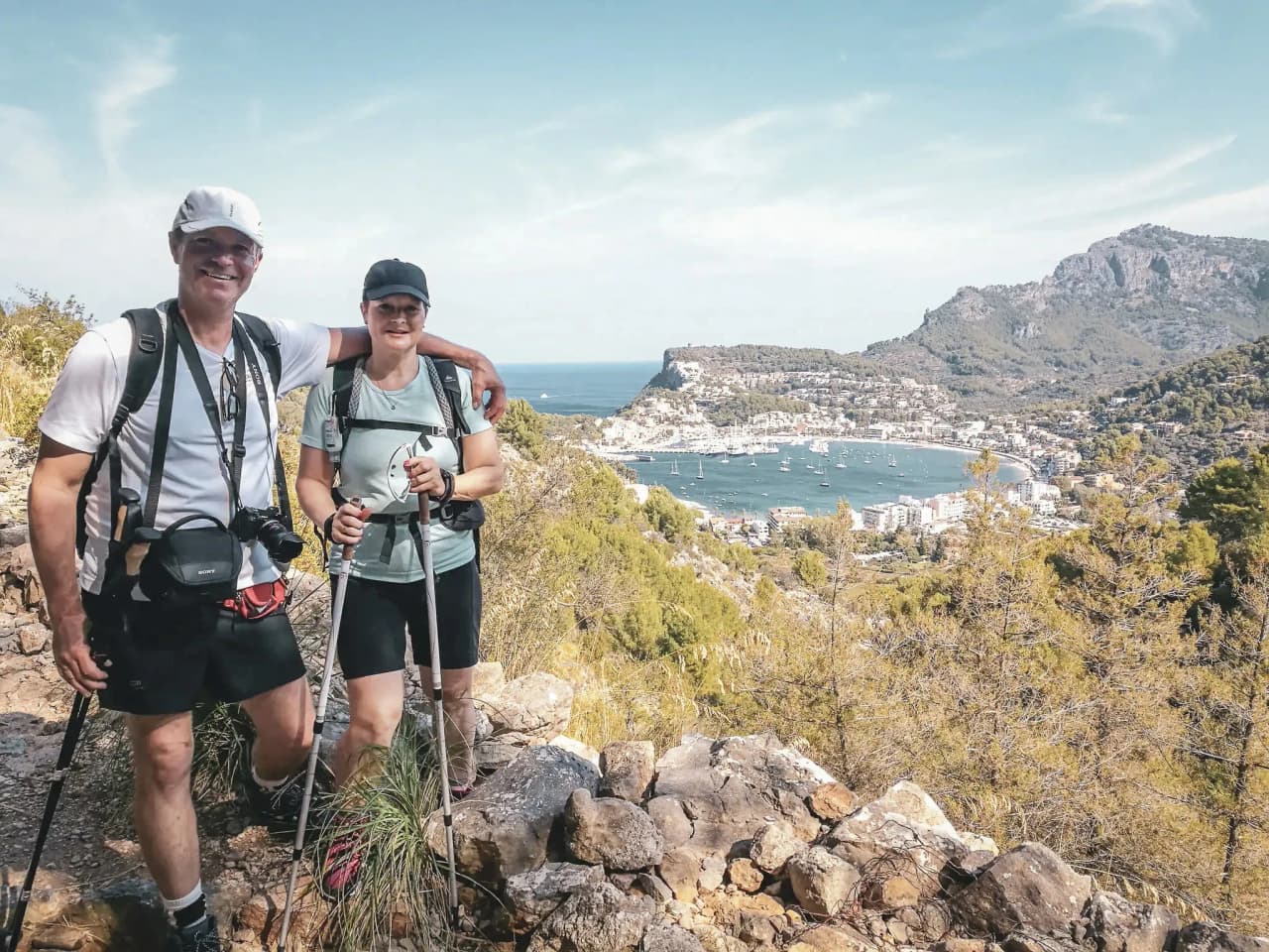 Couple en randonnée avec vue panoramique sur la côte de Majorque, entourés de nature verdoyante.
