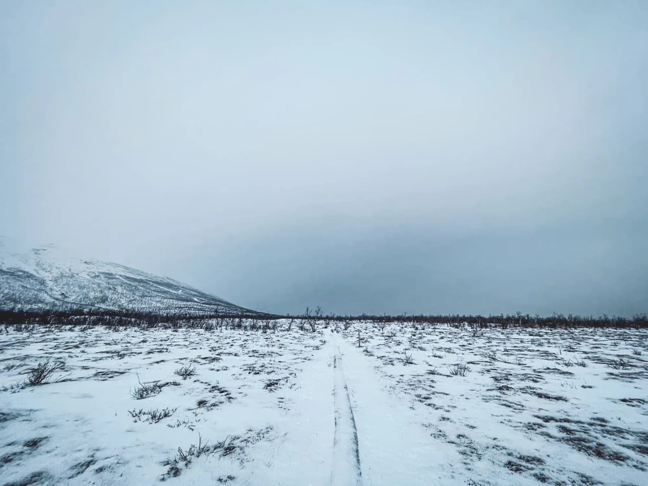 Een besneeuwd Kungsleden landschap met bergen in de verte onder een grijze hemel.