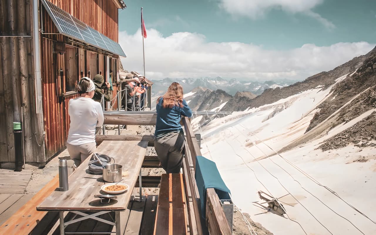 A group of hikers admiring the Aletsch glacier from a sunny alpine hut.