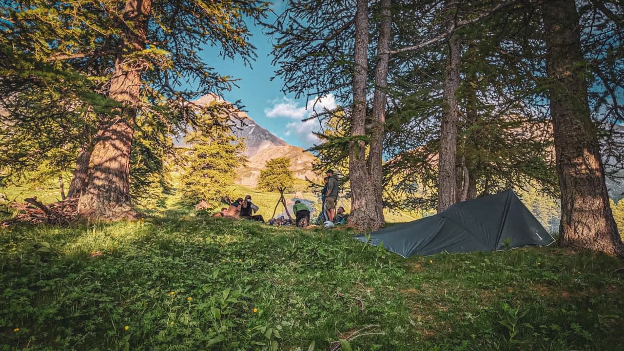 Un groupe pratique la survie en pleine nature, entouré de montagnes et de verdure, ambiance conviviale.