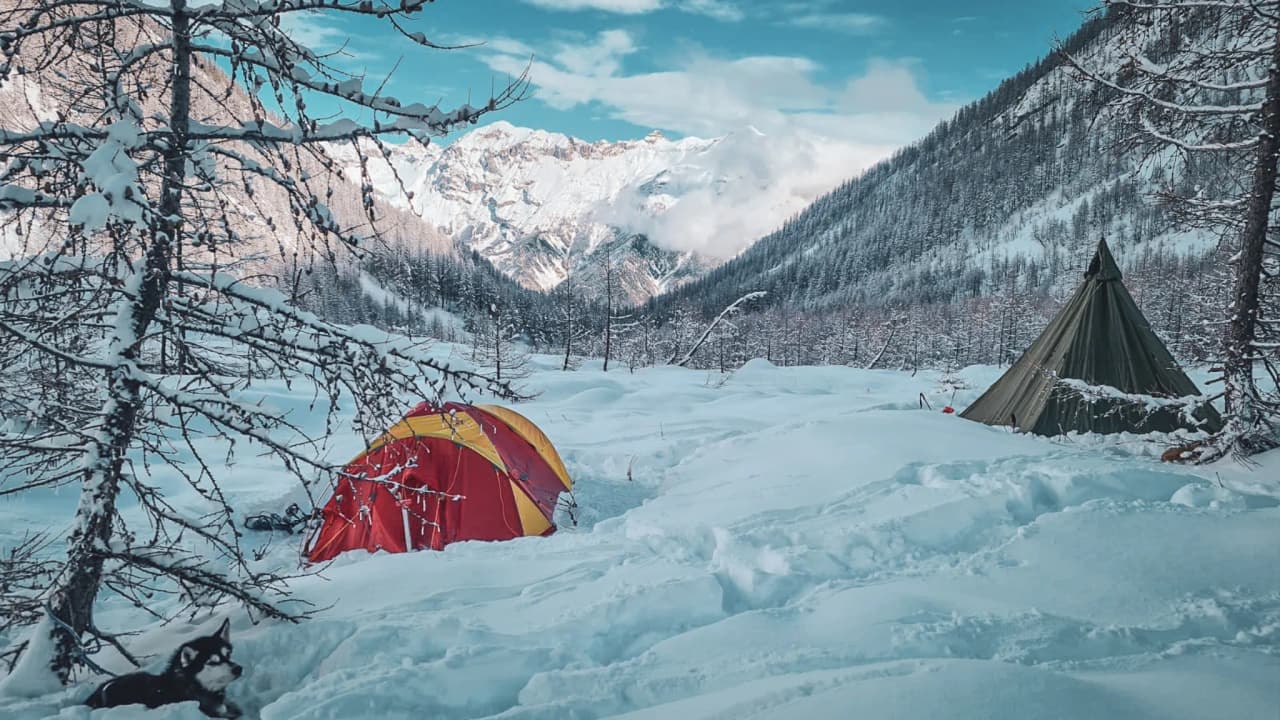 Kleurrijke tenten in een besneeuwd landschap van de Écrins, met majestueuze bergen op de achtergrond.