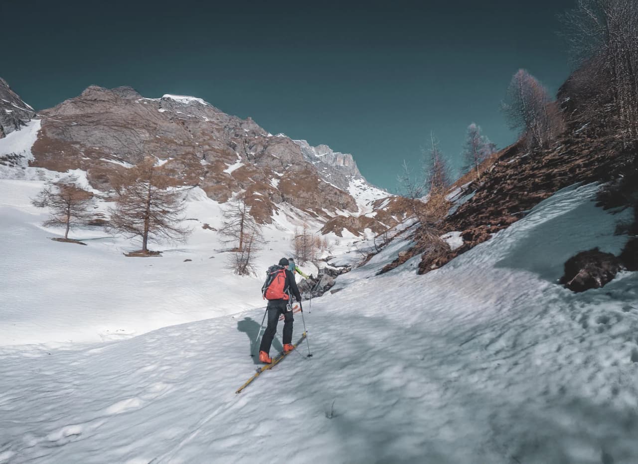 Un skieur en randonnée sur des pentes enneigées, entouré de paysages montagneux majestueux.