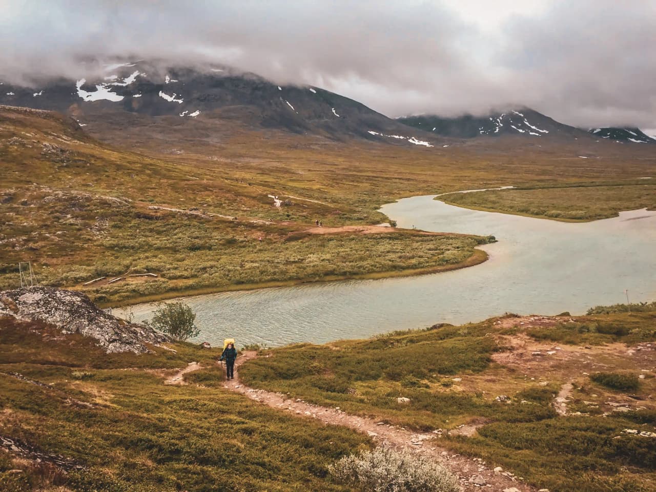 A hiker on a verdant path, revealing majestic mountains and sparkling liquid.
