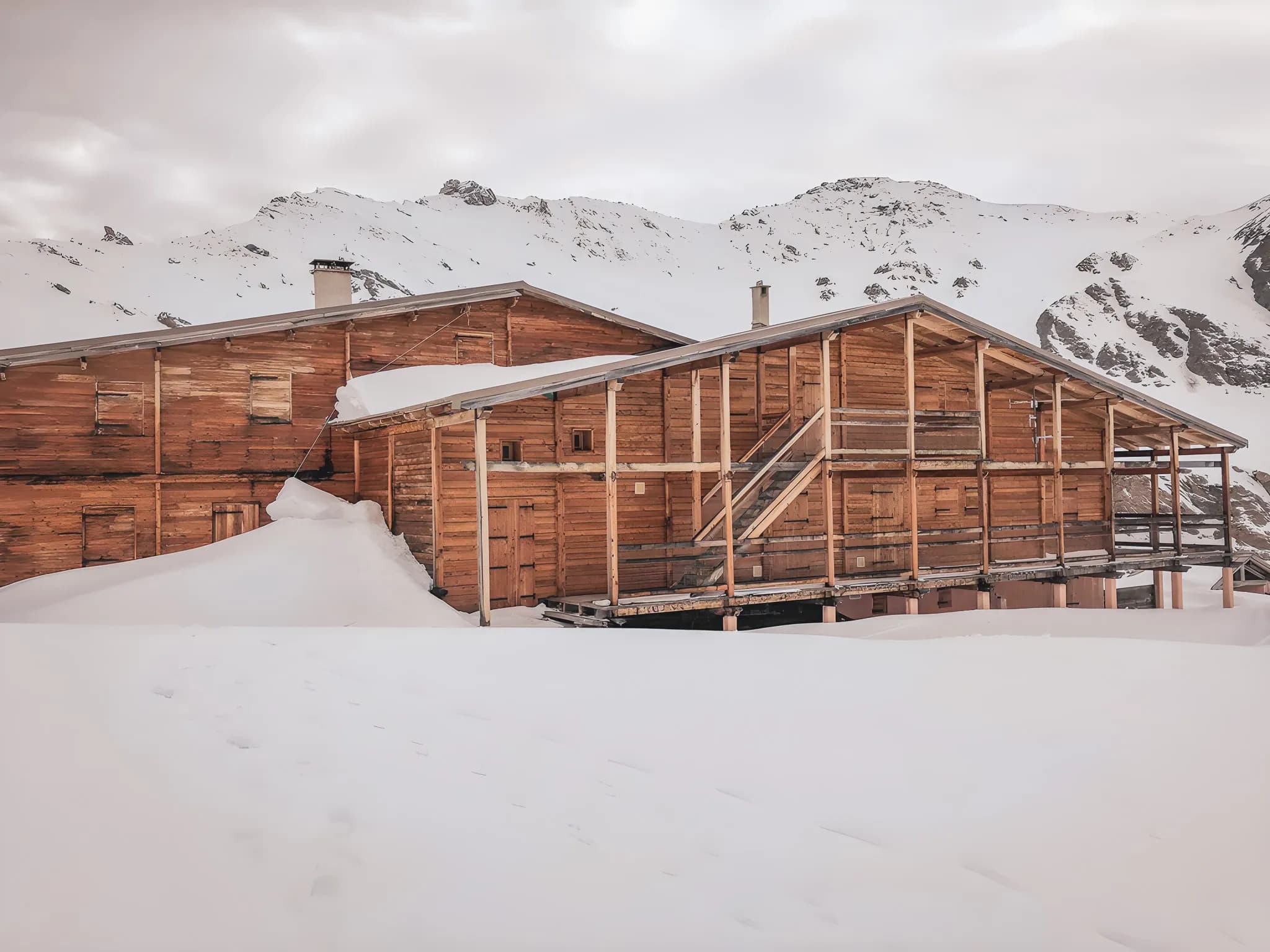 A wooden Mountain hut nestled in the snow, surrounded by majestic snow-capped mountains. Escape guaranteed.