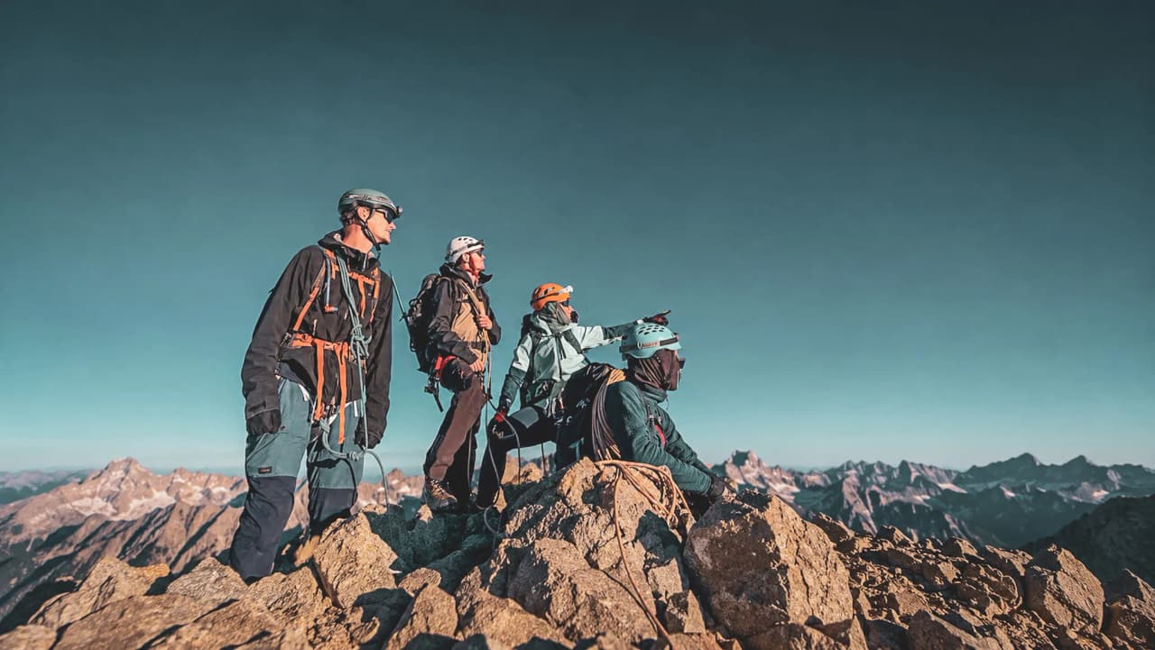 Groupe d'alpinistes au sommet, admirant un panorama montagneux sous un ciel ensoleillé.