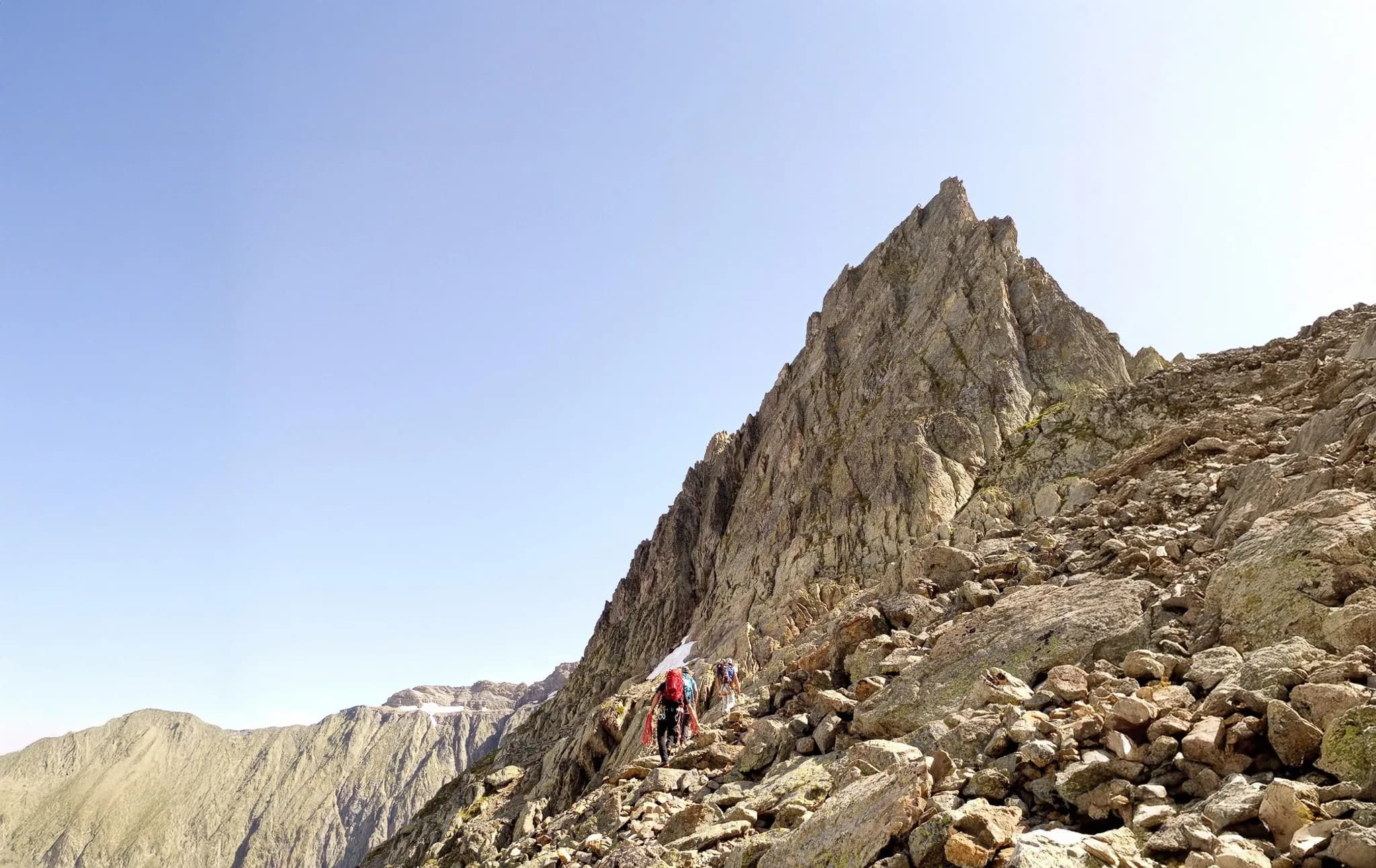 Un groupe d'alpinistes grimpe une arête rocheuse avec le Mont Blanc en toile de fond.