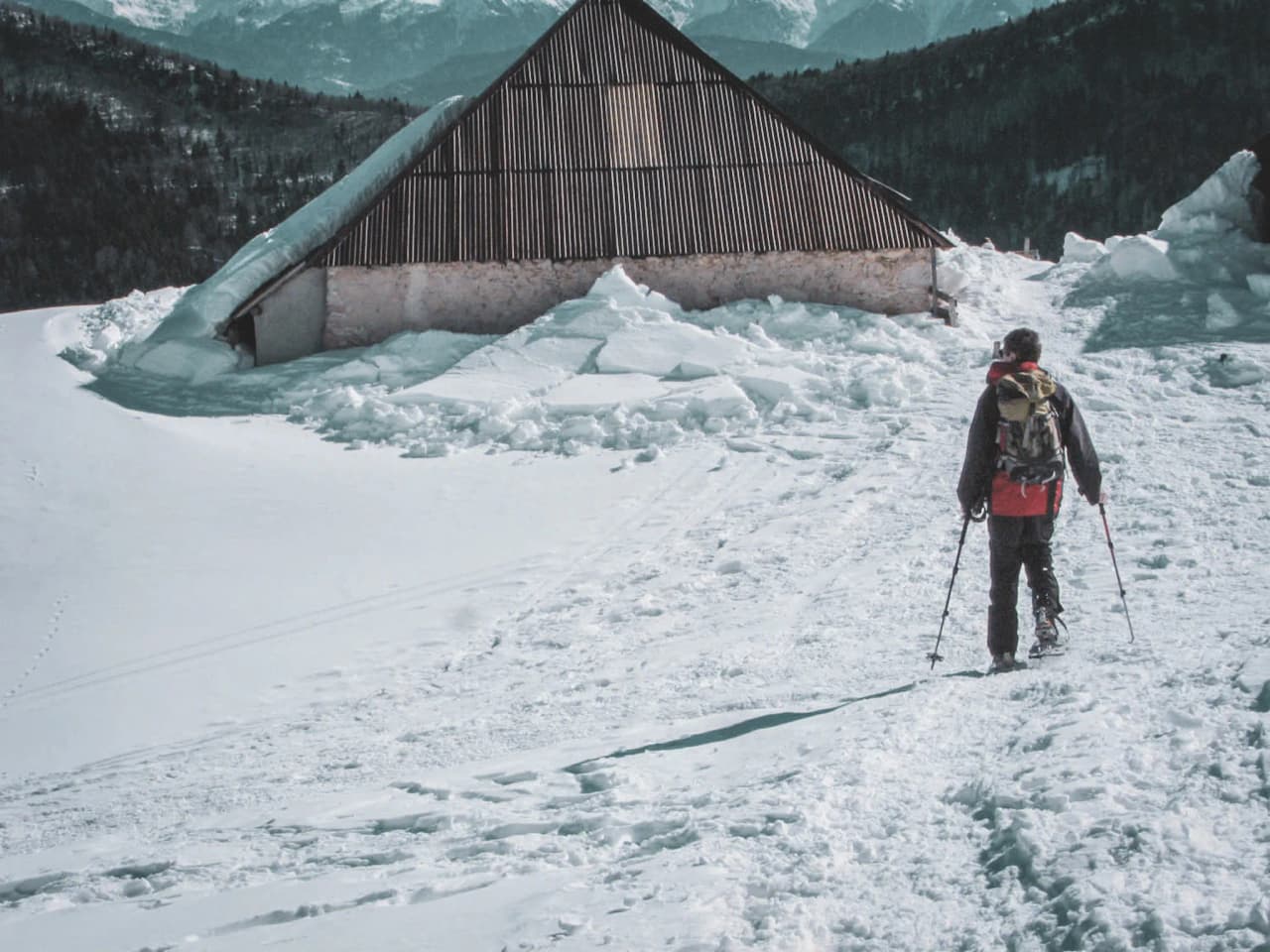 Randonneur en raquettes s'avançant vers un chalet enneigé dans les montagnes des Bauges.