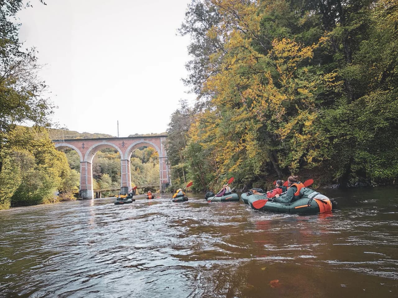 A group of packrafts cruising peacefully under a viaduct in the heart of the Ardennes forests.