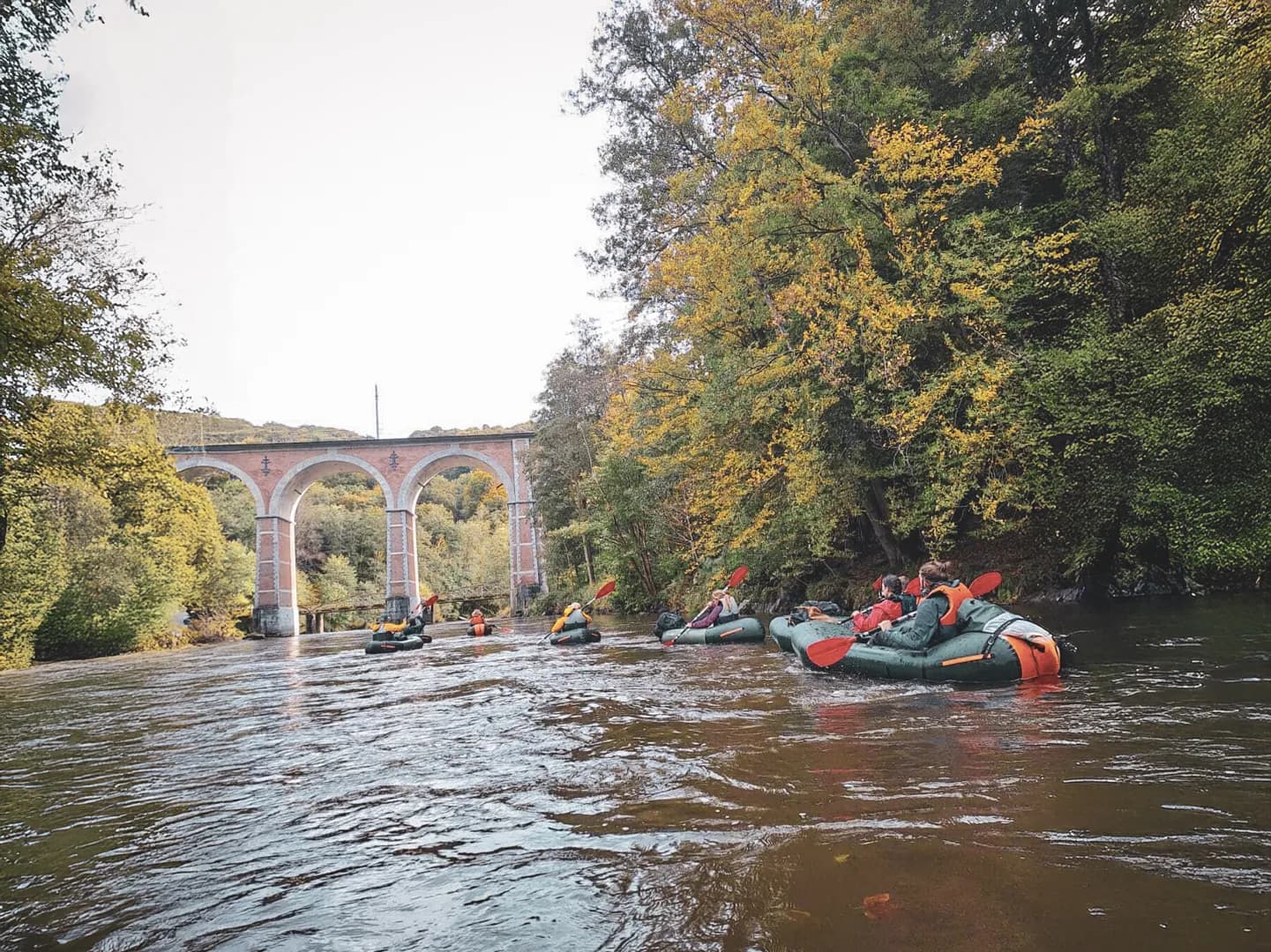 A group of packrafts cruising peacefully under a viaduct in the heart of the Ardennes forests.