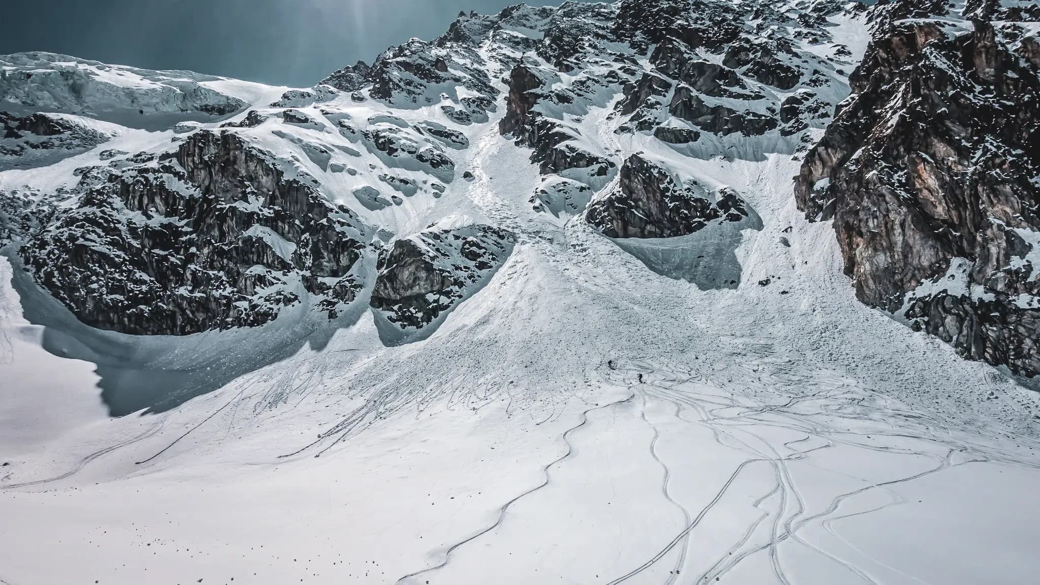A snow-covered Alpine landscape, dominated by majestic mountains with steep, snow-covered slopes. Ski tracks snake across the immaculate surface of the snow, testifying to a long tradition of skiing.