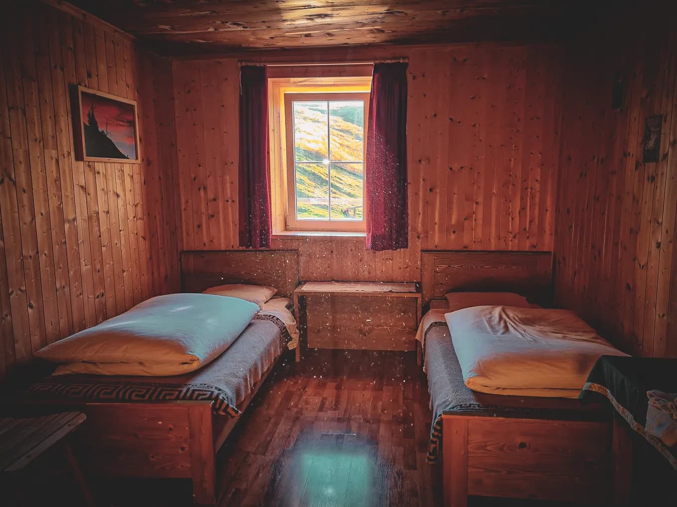 A wooden bedroom, with light wood-panelled walls and ceiling, creates a warm and welcoming atmosphere. Two single beds are lined up, each with tidy sheets and pillows. Between the beds,