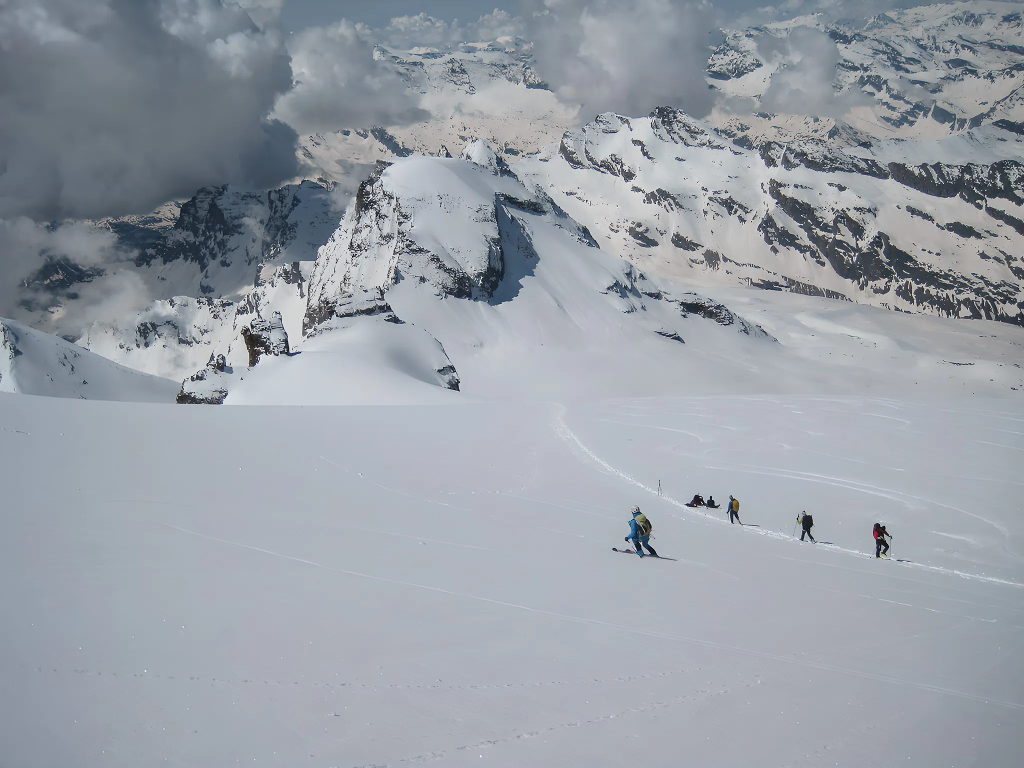 Cinq skieurs traversent un vaste champ de neige, entourés de majestueuses montagnes alpines.