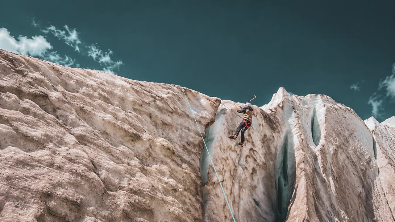 Un alpiniste en pleine ascension sur un glacier, entouré de paysages majestueux des Écrins.
