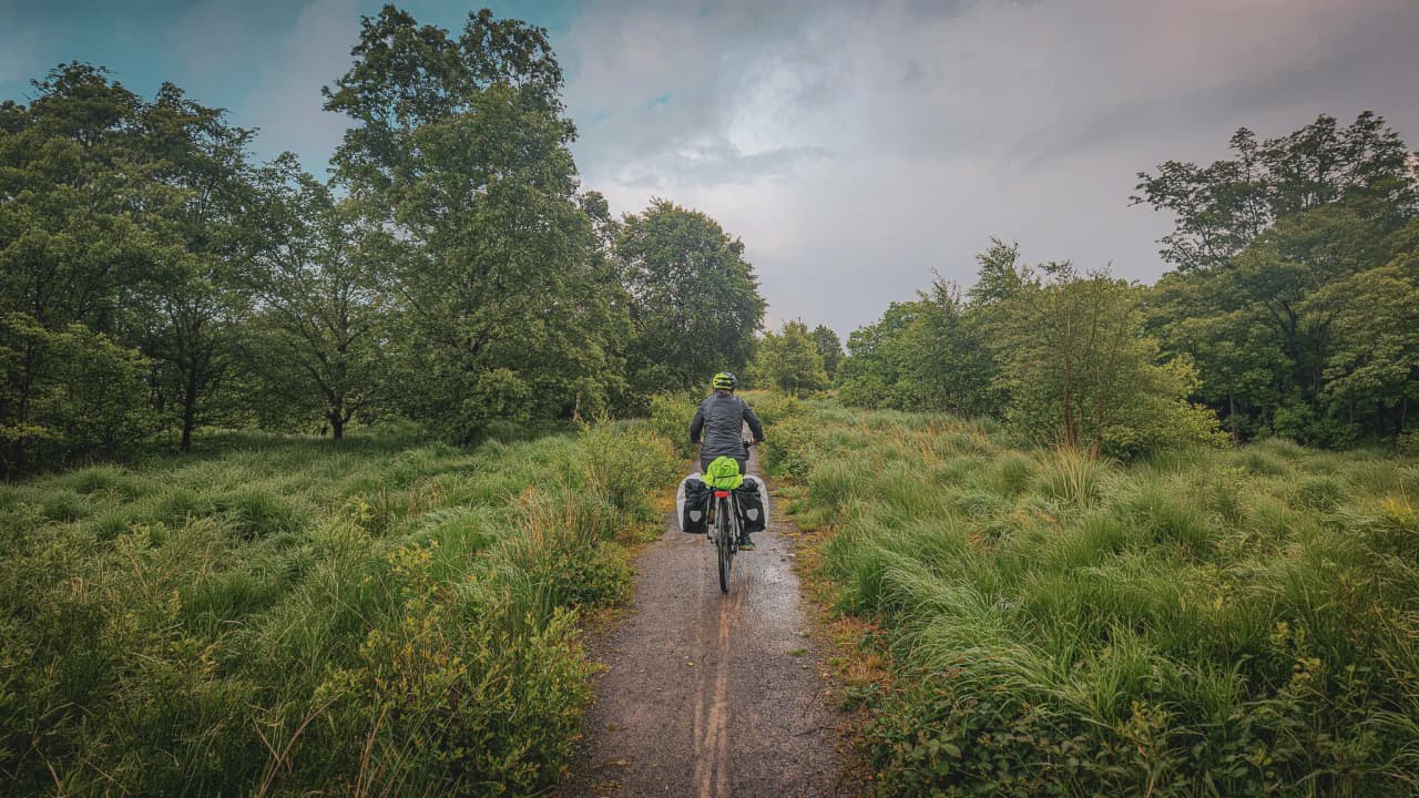 Een fietser verkent een groen pad onder een bewolkte hemel, een inspirerend natuuravontuur.