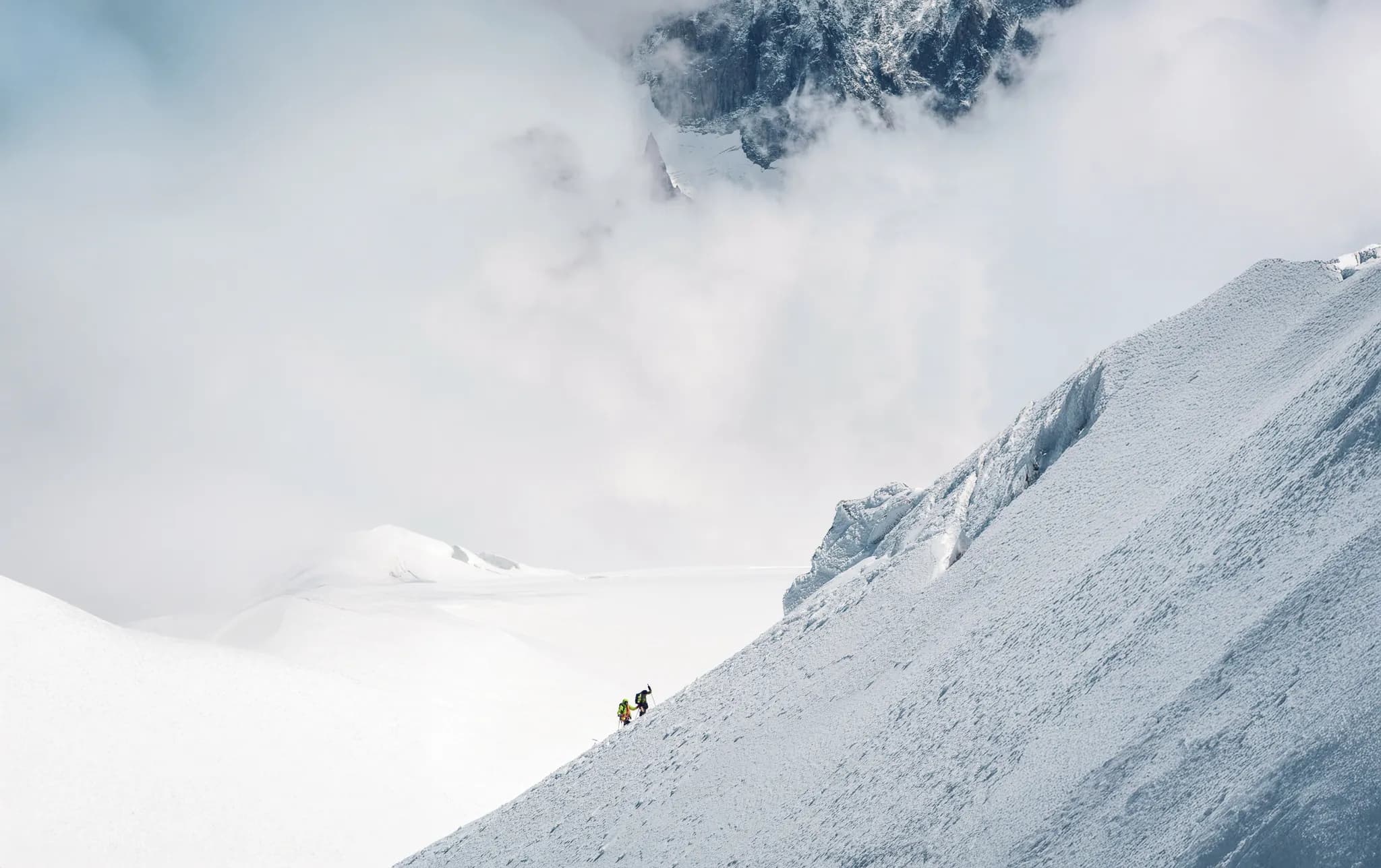 Deux alpinistes gravissent une pente enneigée sous un ciel nuageux, au Mont Blanc. Aventure garantie !