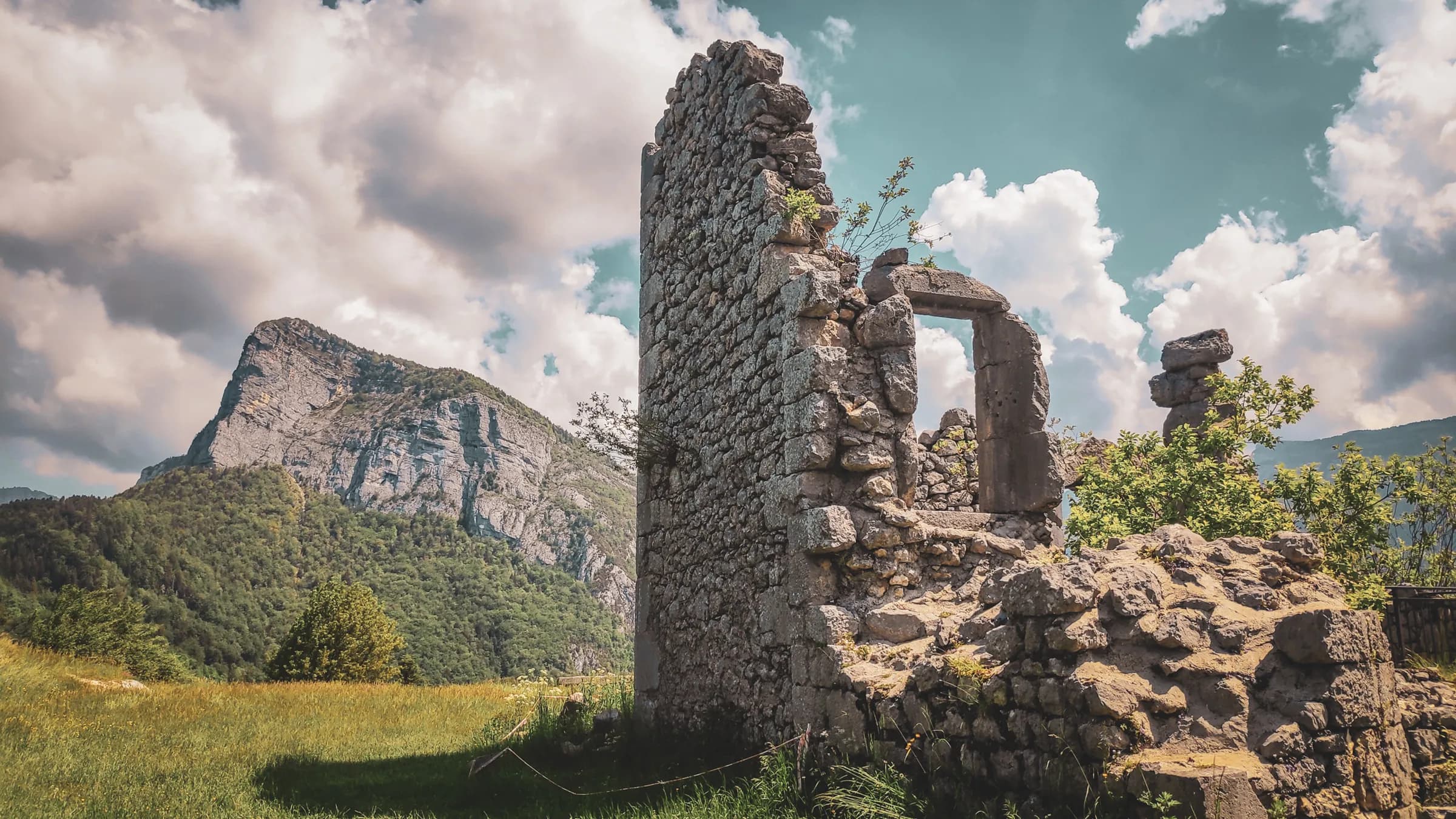 Ruines mystérieuses au cœur des Alpes, entourées de verdure et de sommets majestueux.
