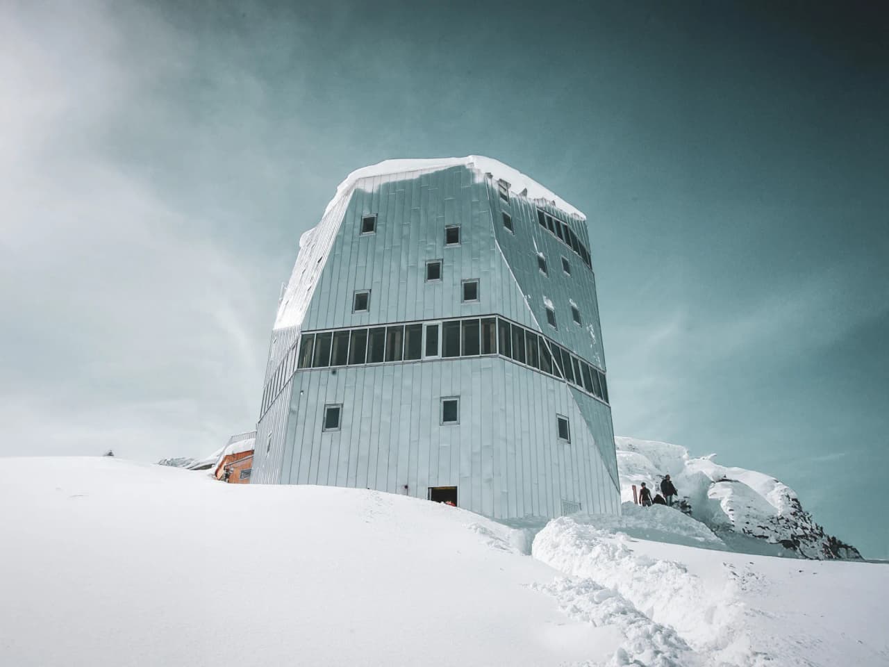Modern mountain hut on dazzling snow, surrounded by majestic Alpine peaks.
