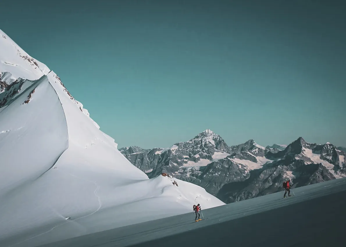 Skiers advance on immaculate snow, facing the majestic peaks of the Alps.