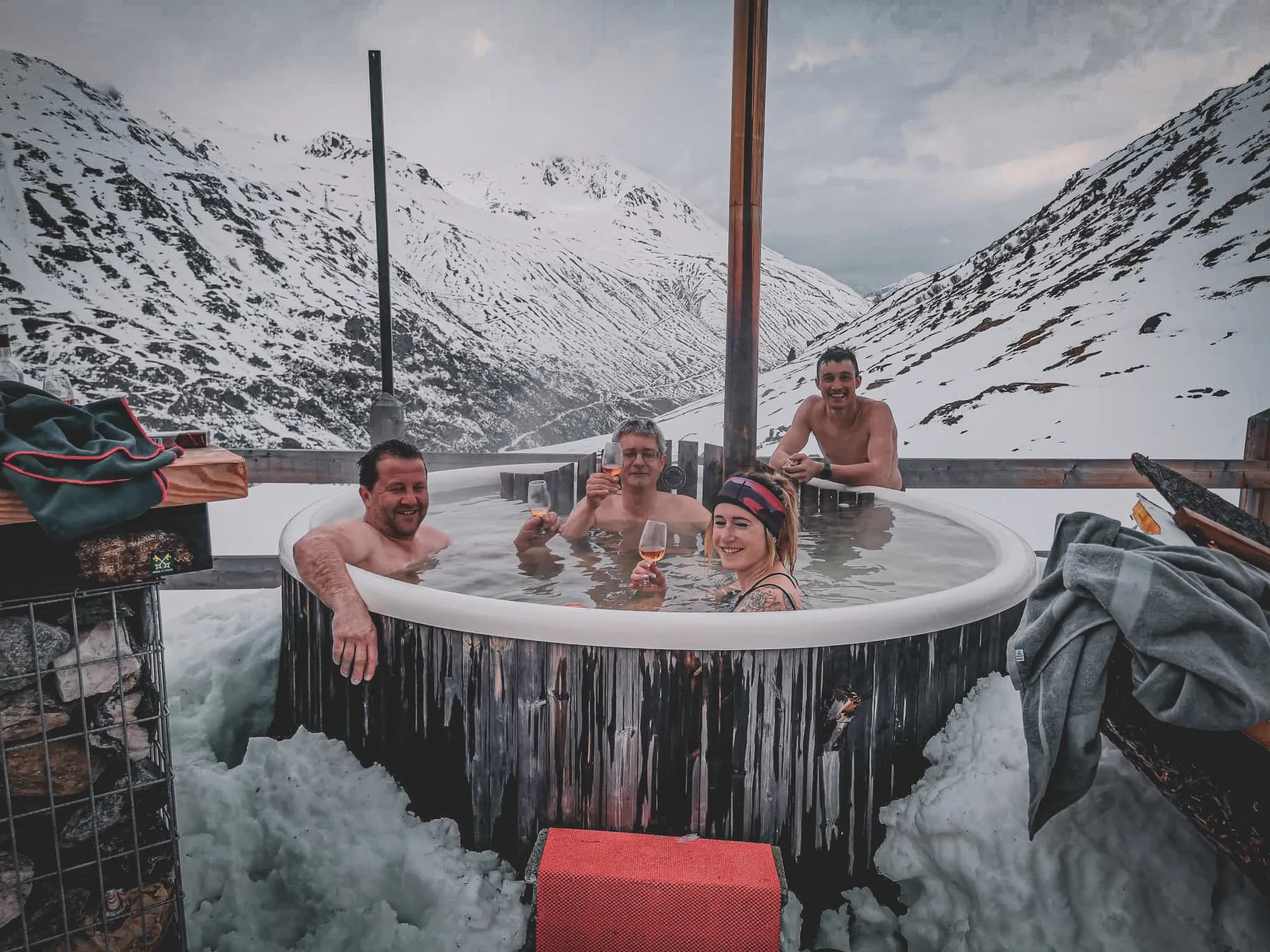 A group of four friends relaxing in a Jacuzzi in the heart of nature, surrounded by snow-capped mountains.