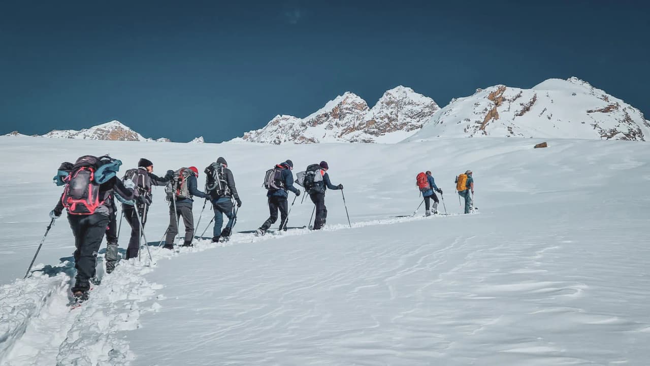 Groupe de randonneurs en raquettes, neige immaculée, montagnes majestueuses en arrière-plan.