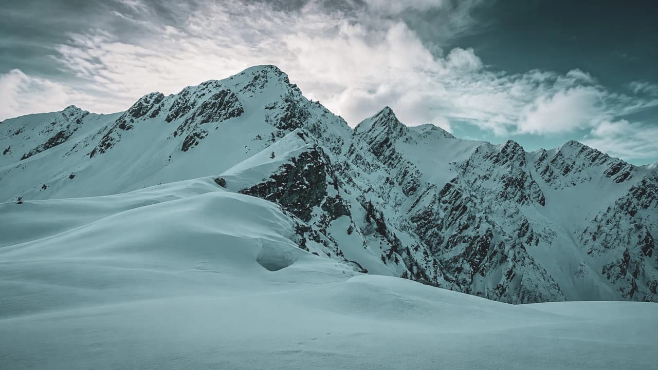 A majestic alpine landscape, snow-capped mountains beneath a cloudy sky – an invitation to adventure.