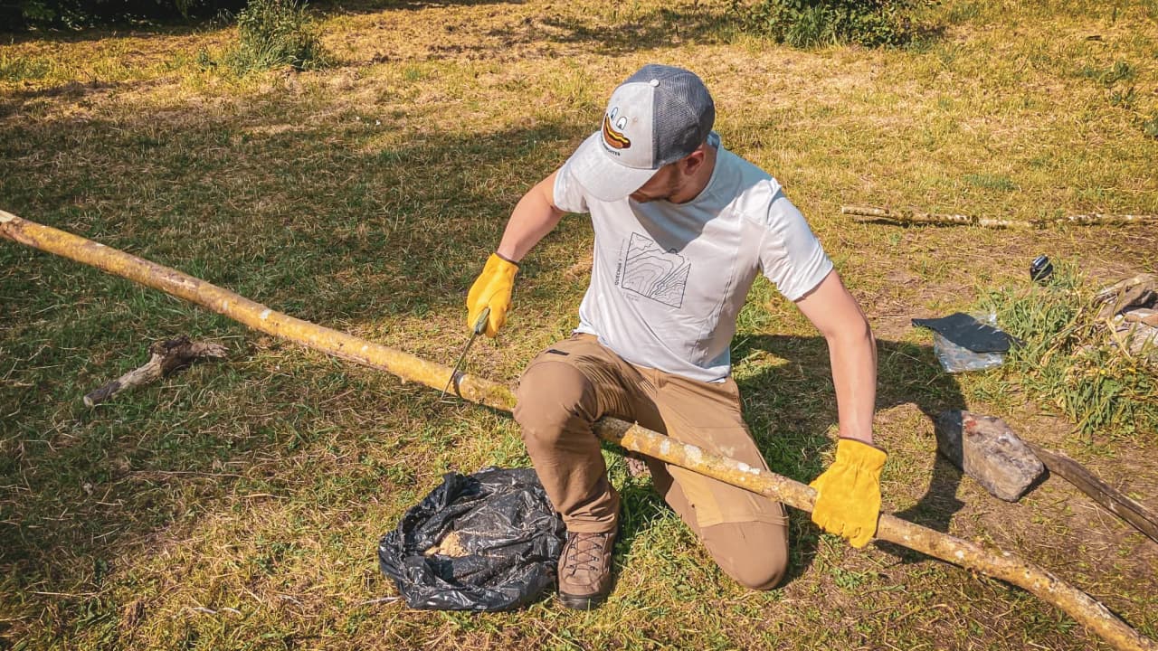 Un participant à un stage de survie en Ardenne belge, préparant un bâton avec soin en pleine nature.