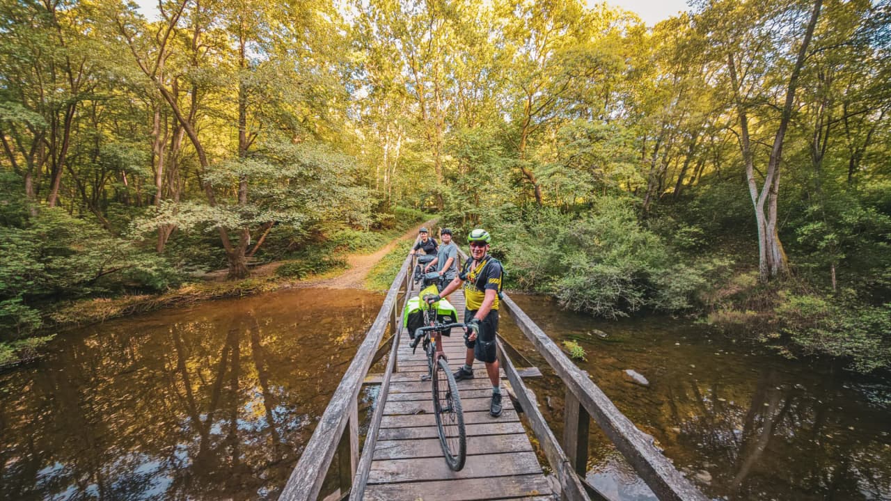 Three cyclists on a wooden bridge, surrounded by the greenery of the Ardennes forests.