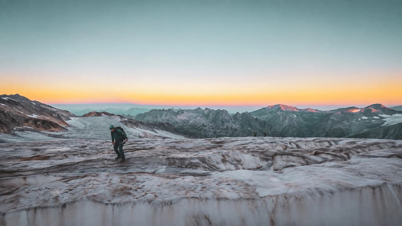 Alpiniste sur un glacier au coucher du soleil, avec des sommets majestueux en arrière-plan.