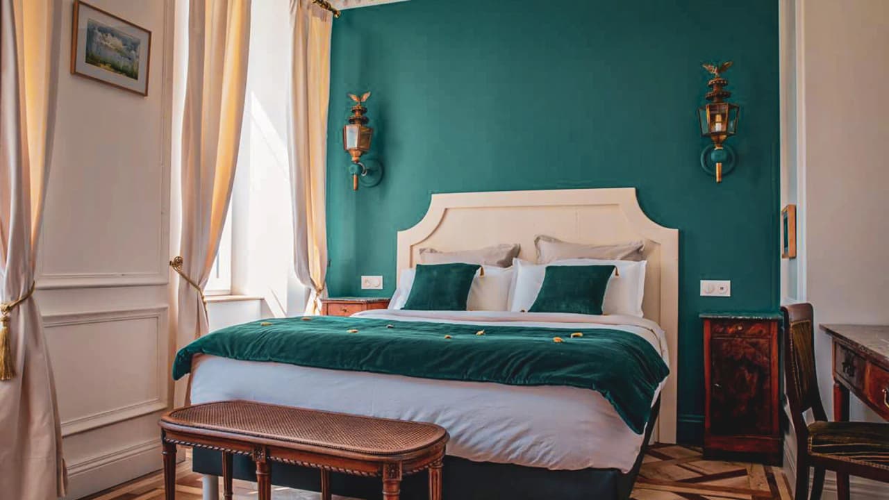 An elegant room with a cosy bed, teal walls and natural light, ideal for relaxing after an adventure.
