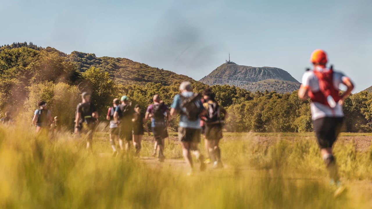 A group of runners on a trail with the Auvergne volcanoes in the background.