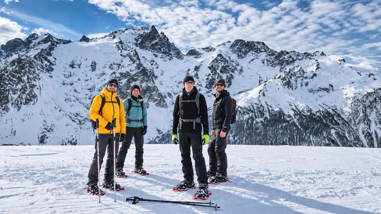 Een groep avonturiers op sneeuwschoenen op een besneeuwd plateau, met het majestueuze Écrins-gebergte op de achtergrond.