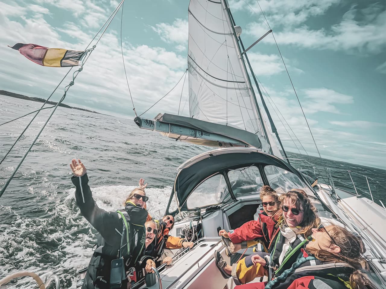 Groupe souriant en voilier sur les eaux du Pays de Galle, paysages marins captivants.